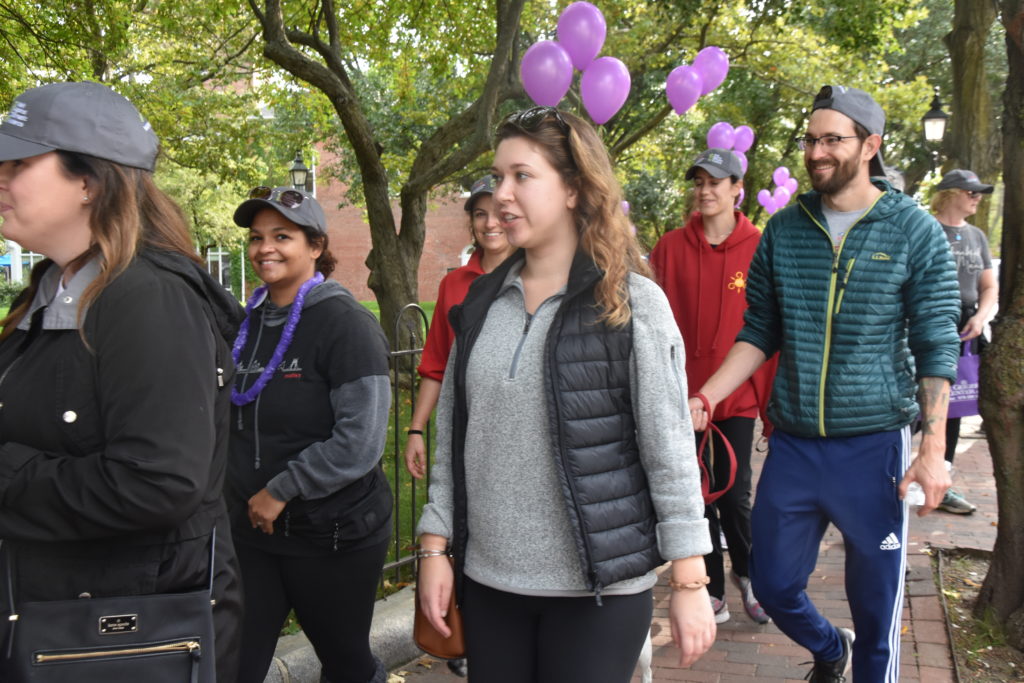 Group of people smiling and walking on a sidewalk outside, lined with balloons