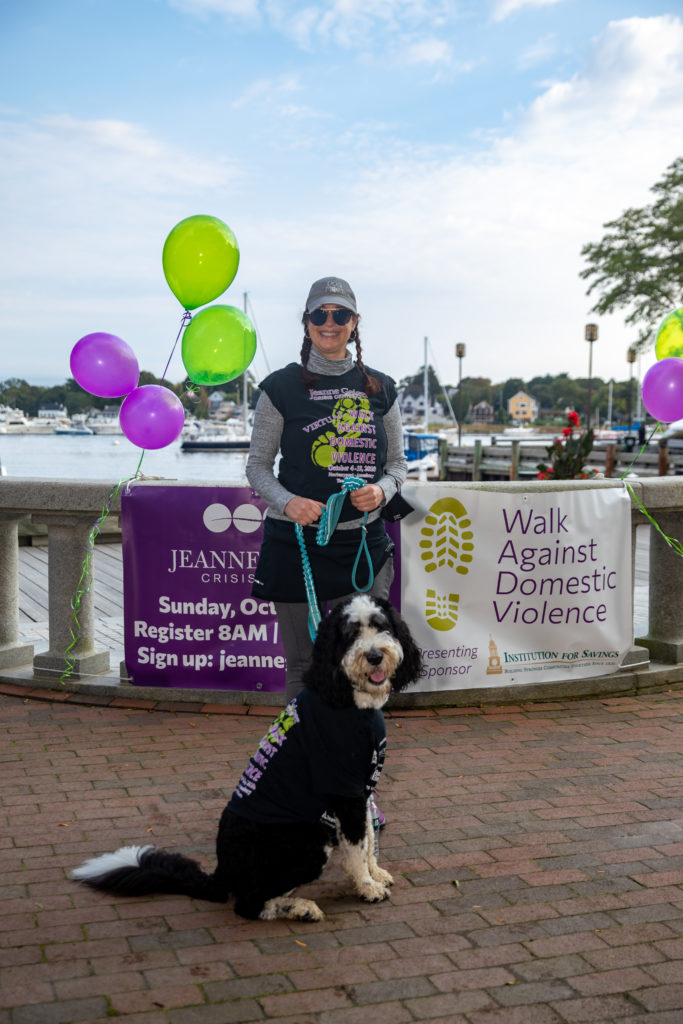 Smiling woman with black and white dog stands in front of banner and balloons.