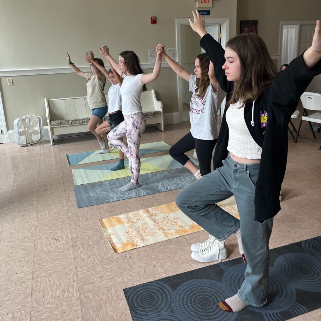 A group of girls on yoga mats raise their hands in a pose