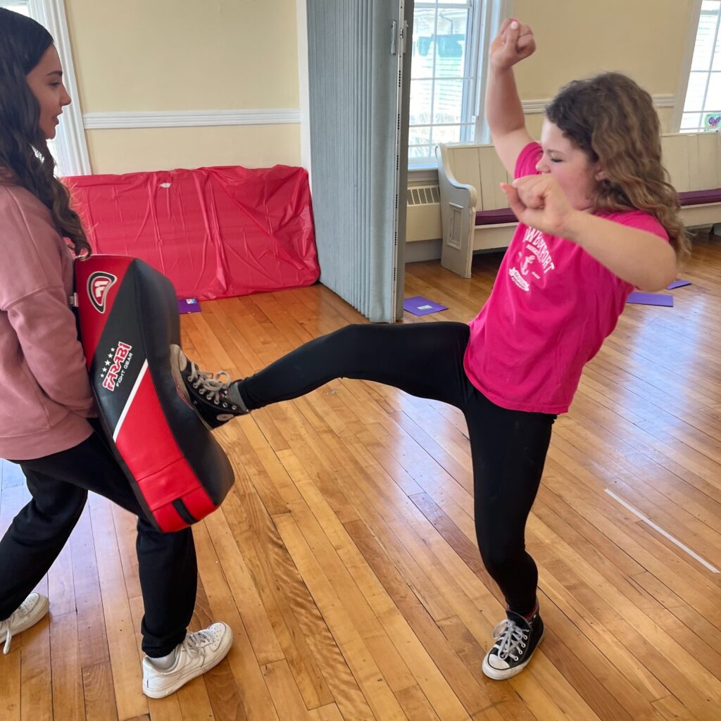 A young girl kicks a padded block in self-defense